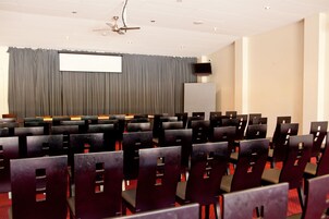 Uma sala de conferências com fileiras de cadeiras, uma tela de projetor e um ventilador de teto.