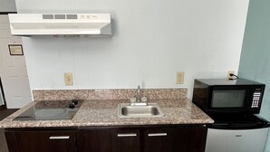 A compact kitchen with a granite countertop, a built-in sink, dark wooden cabinets, a microwave, and a wall-mounted air vent.