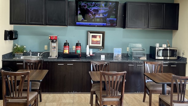 A modern kitchen with dark cabinetry, a flat-screen TV mounted above the counter, and a coffee station with multiple coffee makers.