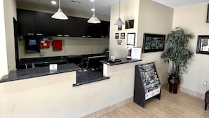 A reception area with a counter, two pendant lights, a potted plant, and a framed certificate on the wall.