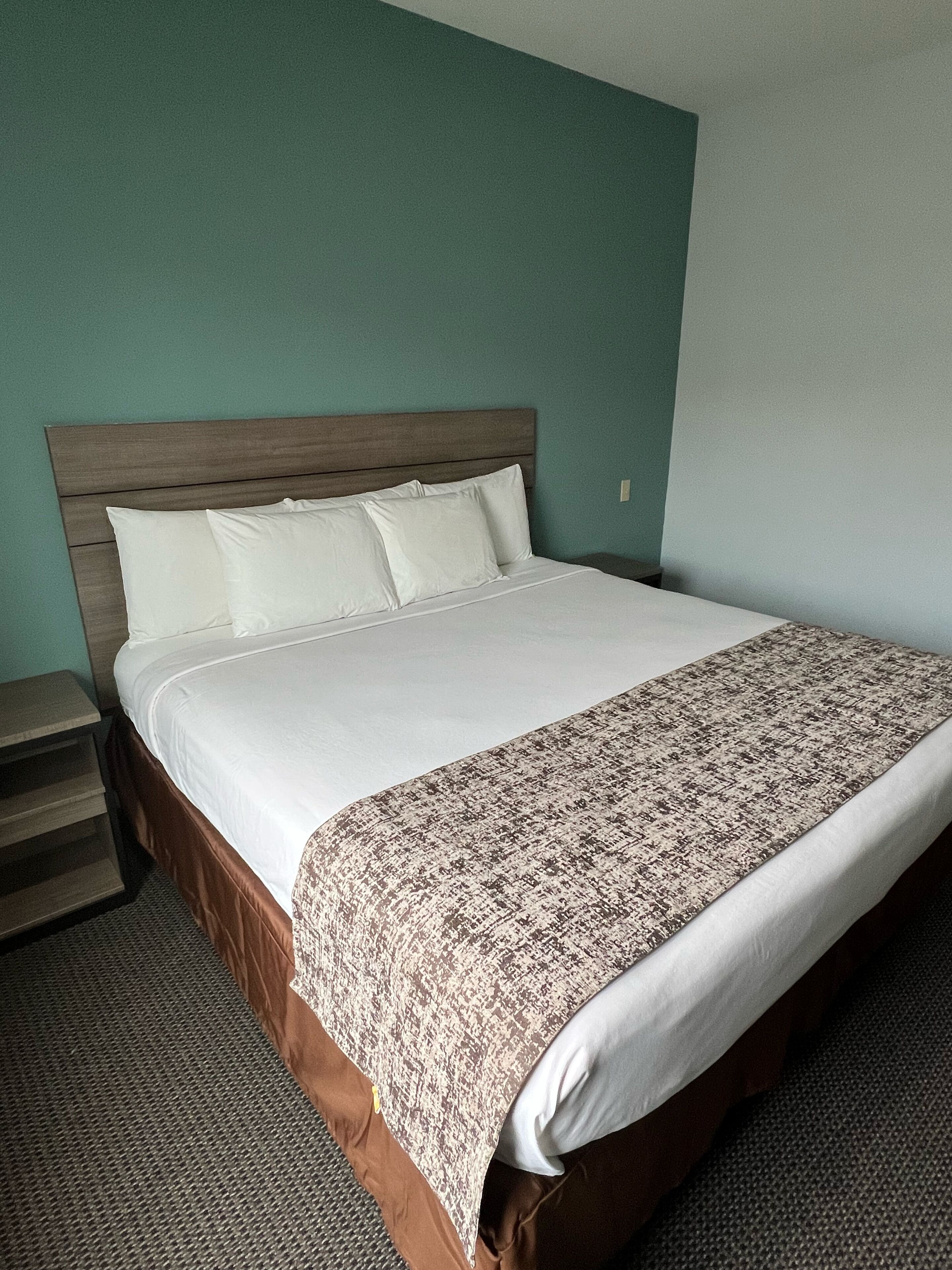 Uma cama bem arrumada com um manta estampada, cabeceira de madeira e mesa de cabeceira com abajur.