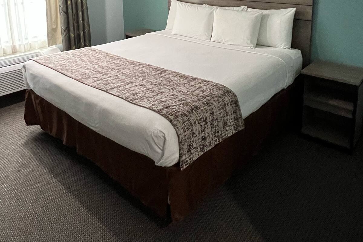 A hotel room with a large bed, a bedside table, and a window with curtains.