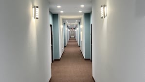 A long, narrow hotel corridor with light blue walls, brown carpet, and recessed ceiling lights.