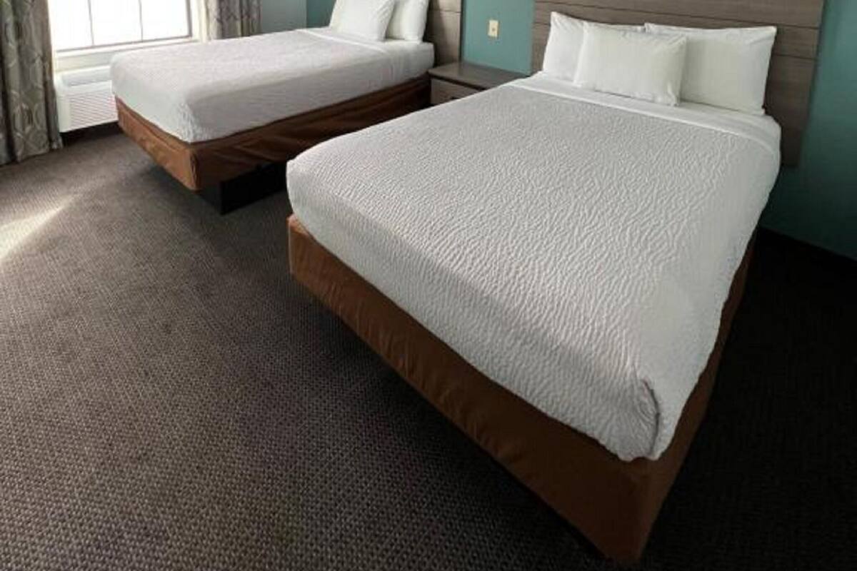 A hotel room with two beds, a window with curtains, and a carpeted floor.