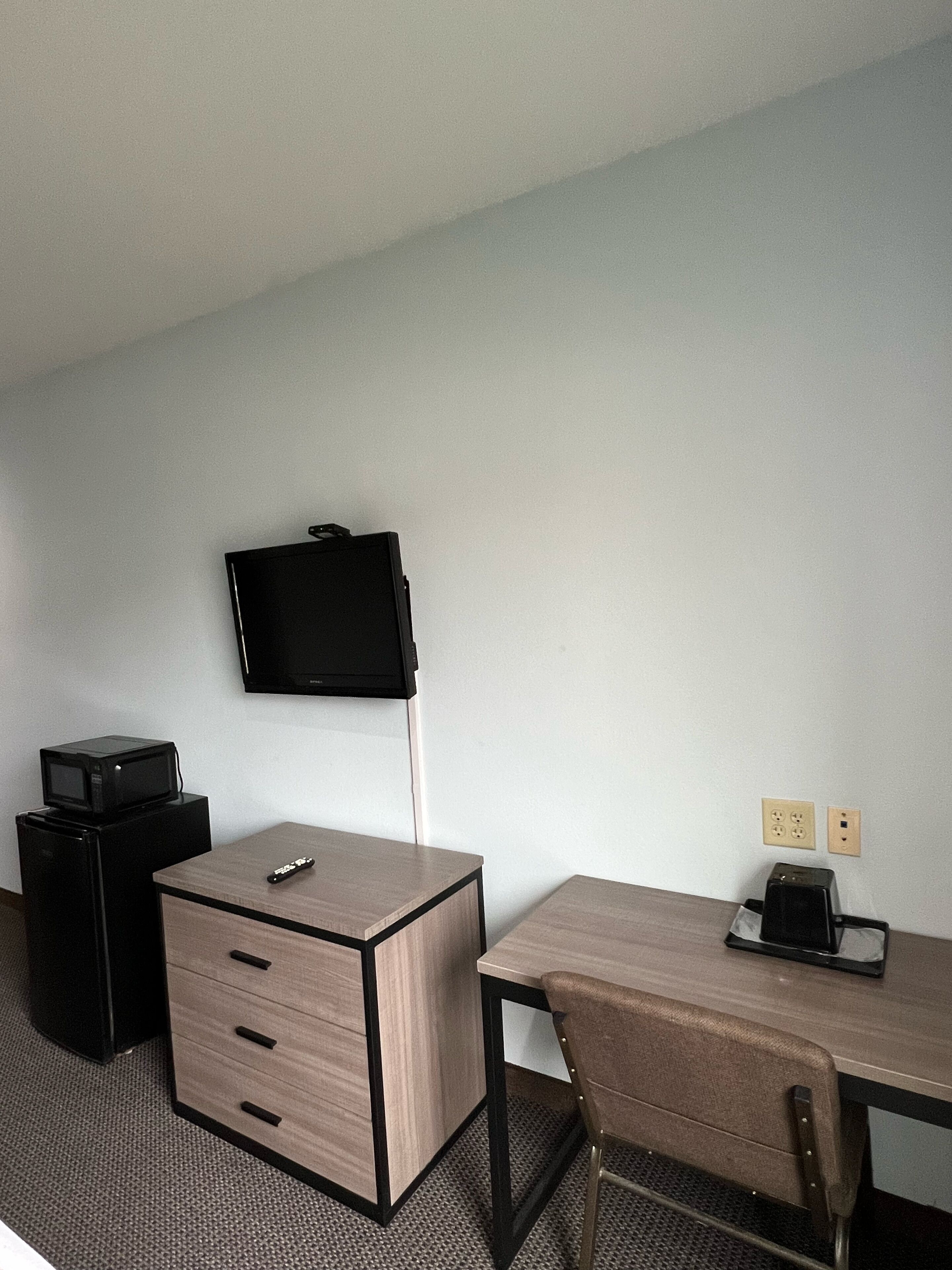 Ein Hotelzimmer mit Schreibtisch, Stuhl, Wandfernseher, Mikrowelle und Toaster auf dem Schreibtisch.