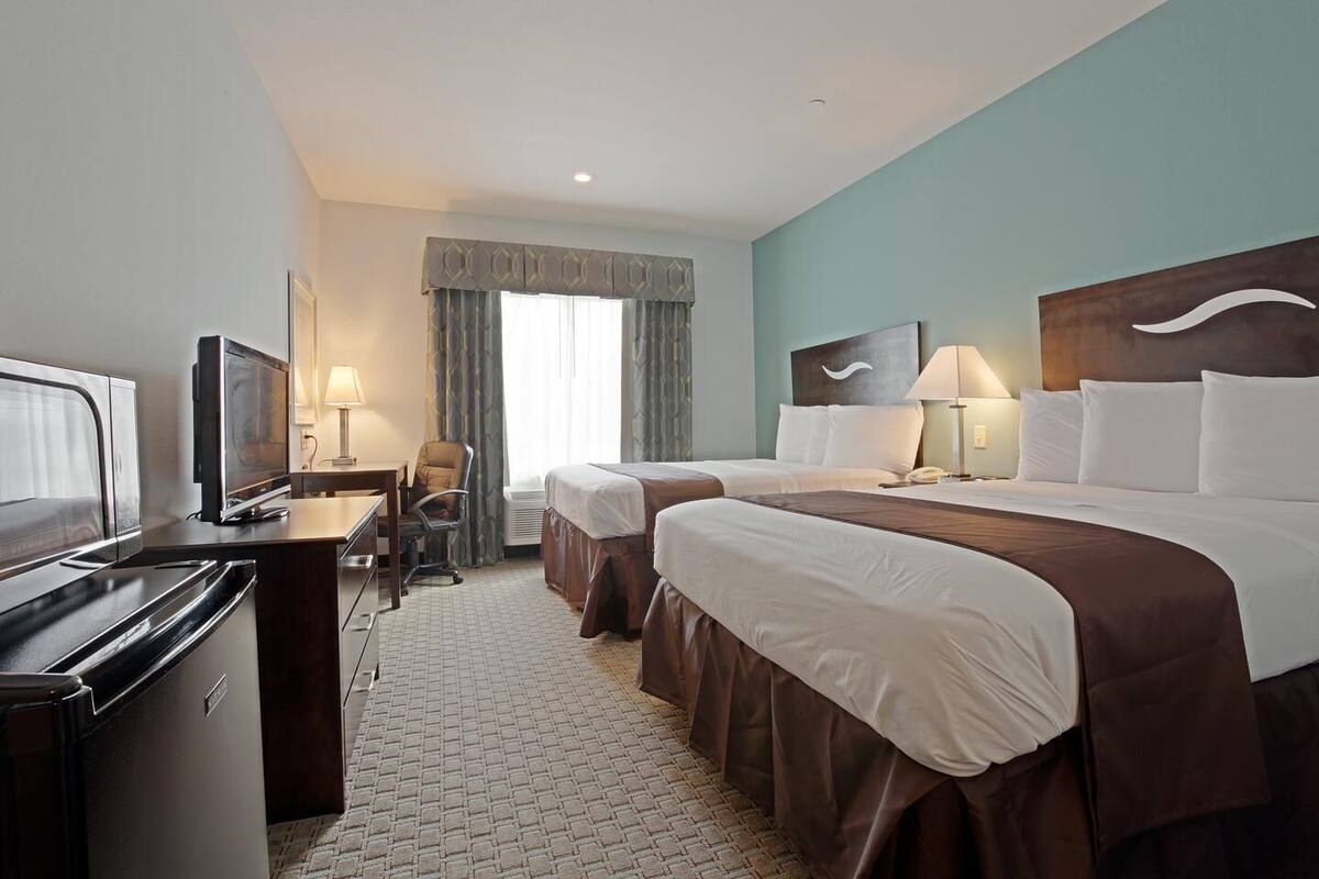 A hotel room with a bed, two bedside tables, a desk with a chair, a television, and a minibar.