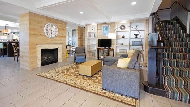 A spacious living room with a fireplace, a large clock, and a staircase. - Country Inn & Suites by Radisson, Texarkana, TX (Texarkana)