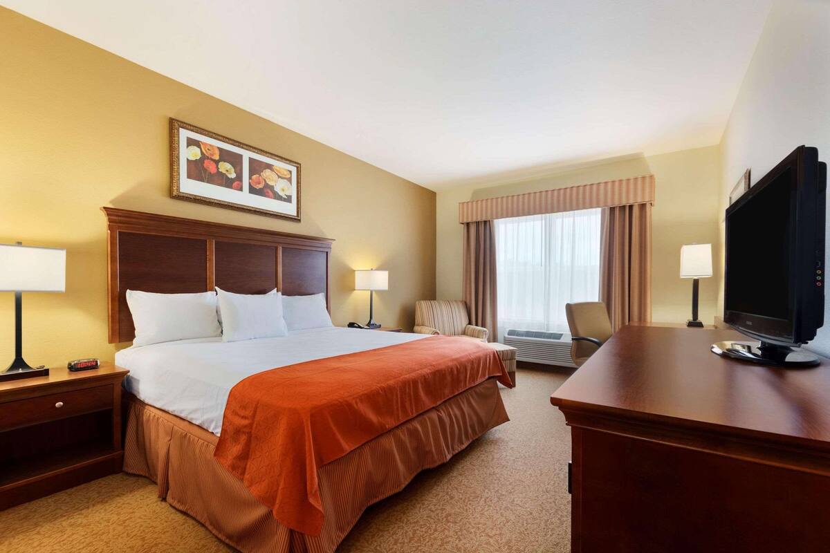 A hotel room with a large bed, two bedside tables with lamps, a television on a wooden desk, a chair, and a window with curtains.