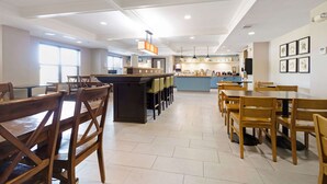 A spacious dining area with wooden tables and chairs, a central bar area, and a kitchen in the background. - Country Inn & Suites by Radisson, Texarkana, TX (Texarkana)