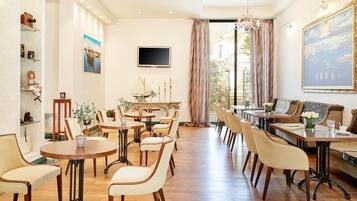 A spacious dining area with multiple tables and chairs, a television mounted on the wall, and a large painting above the seating area.