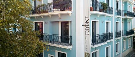 A multi-story hotel with balconies, a sign reading "Boutique Hotel DIONTE", and a tree with autumn leaves in the foreground.