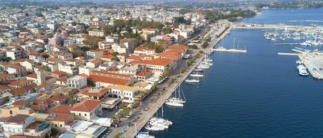 A coastal town with a marina filled with boats, a dense urban area with red-roofed buildings, and a clear view of the sea.