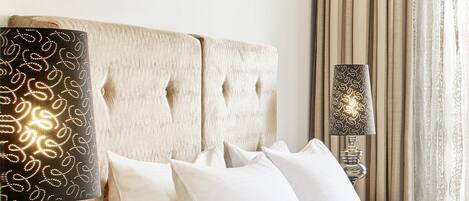 Una cama bien tendida con sábanas y almohadas blancas, un cabecero de madera y dos lámparas de noche con estorbos estampados.