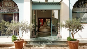 A building entrance with a glass door, a bench, and two potted plants.