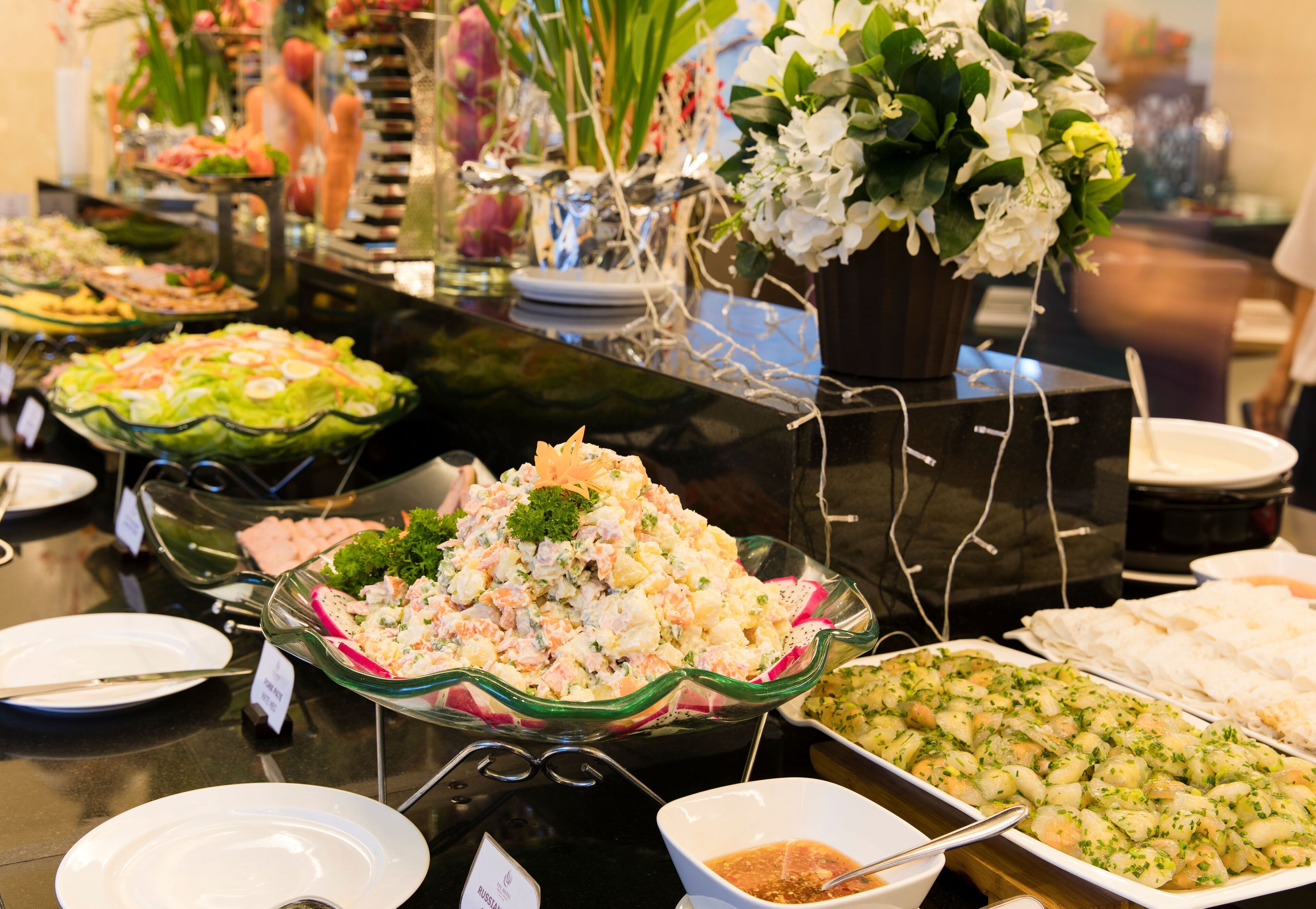 A buffet with various dishes, including salads and seafood, arranged on a table with a glass display case.