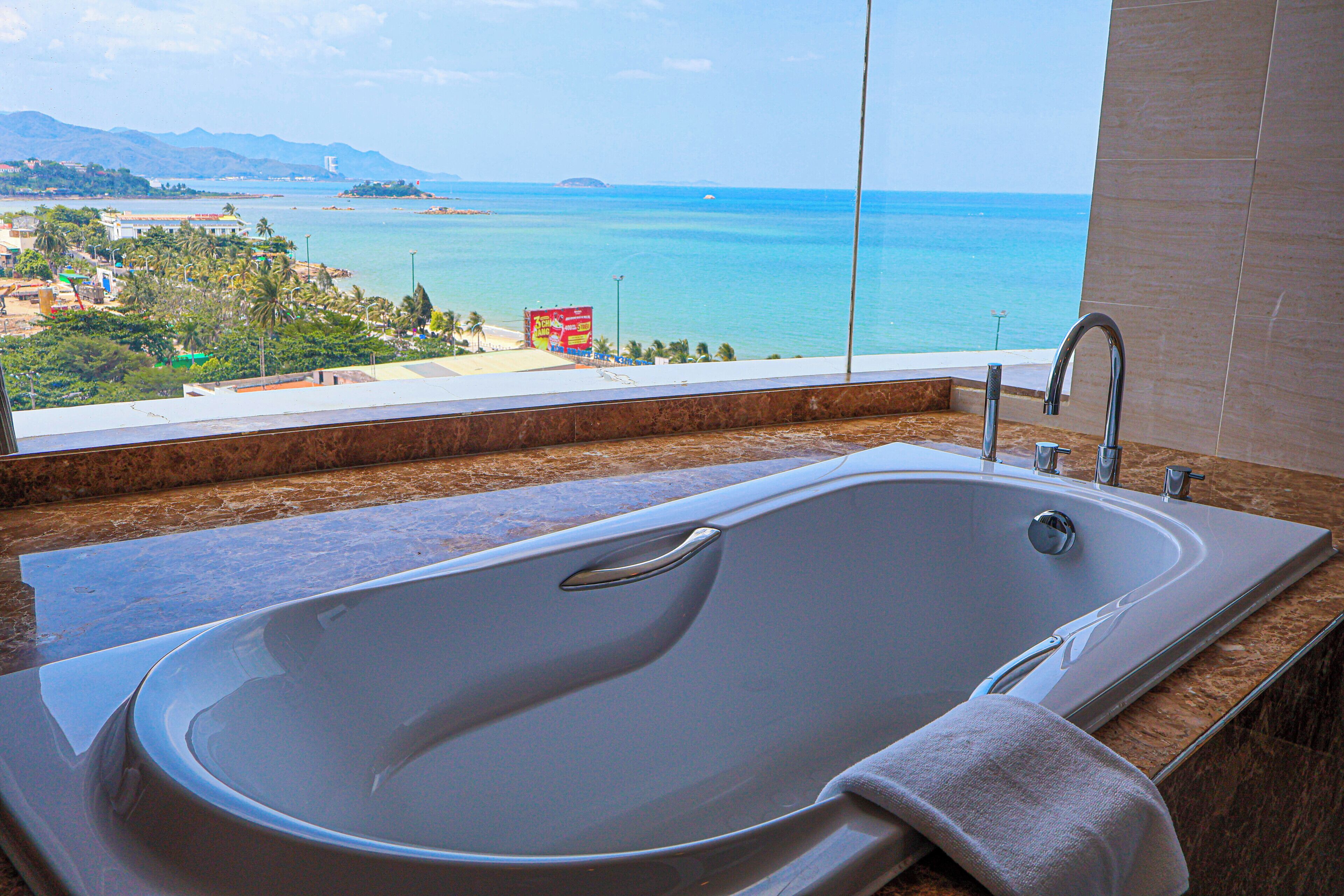 Un baño moderno con una bañera grande, vistas al mar y encimera de mármol.