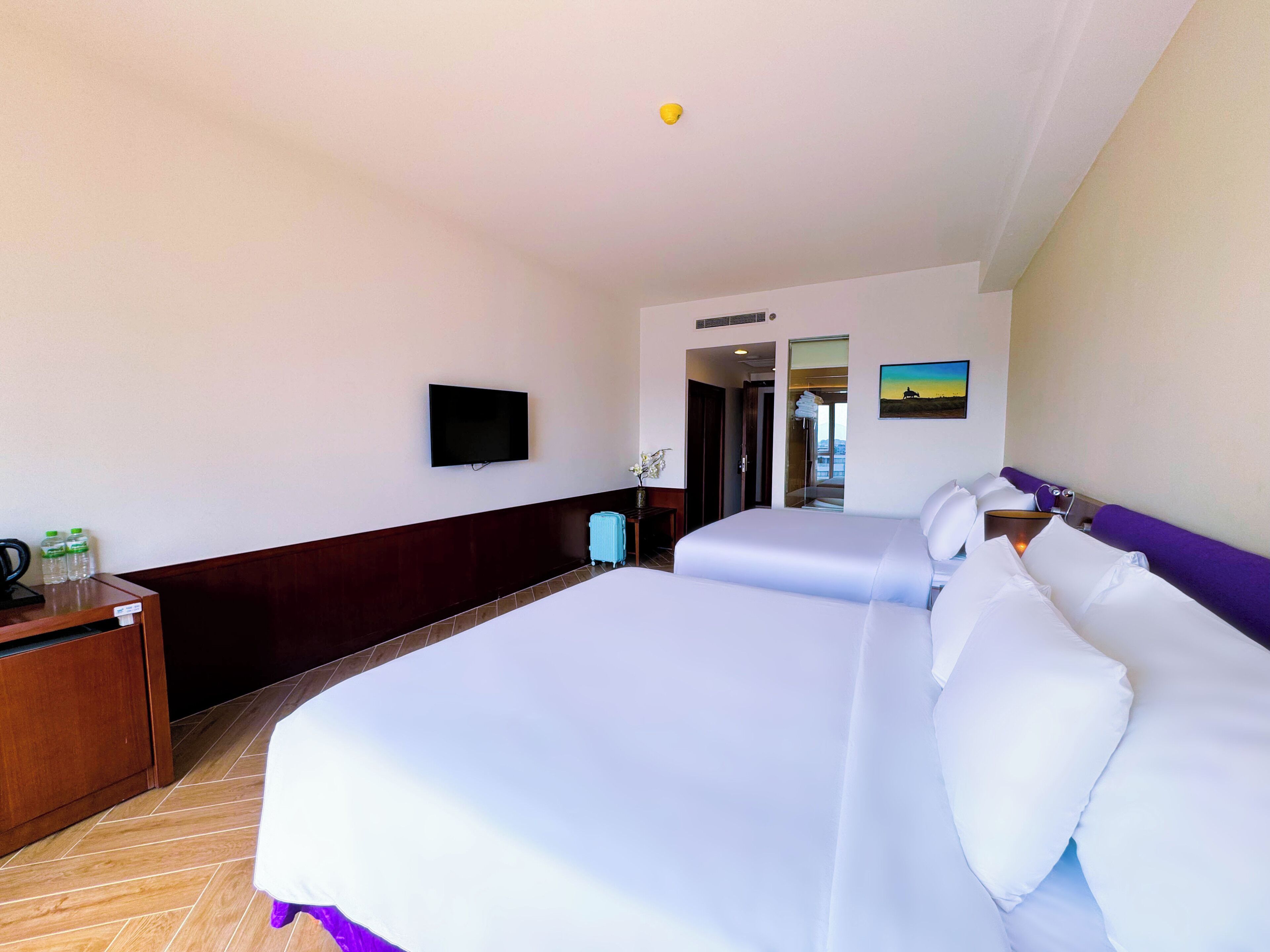 A hotel room with two beds, a television, a desk with a chair, and a view of the outside.