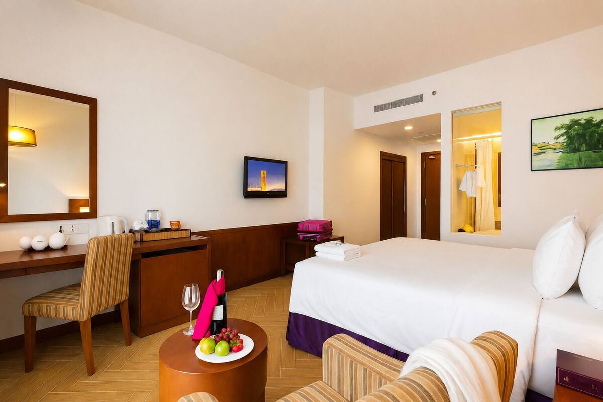 Habitación de hotel con cama, escritorio, silla, televisor, baño y un cuadro en la pared.