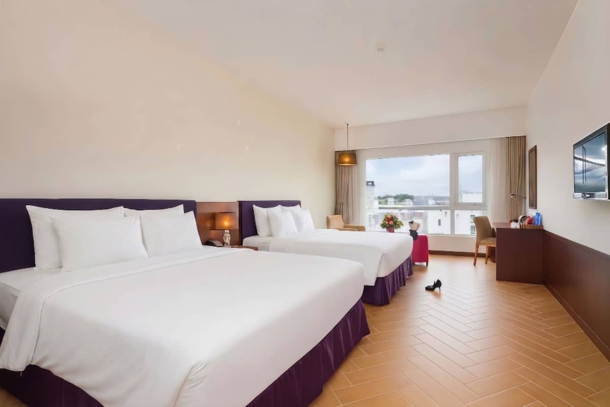 Habitación de hotel con dos camas, un escritorio, una silla, un televisor y un amplio ventanal con vistas.