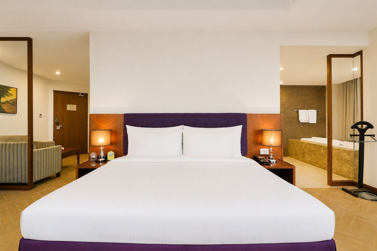 A hotel room with a large bed, bedside tables with lamps, a bathroom with a bathtub, and a mirror.