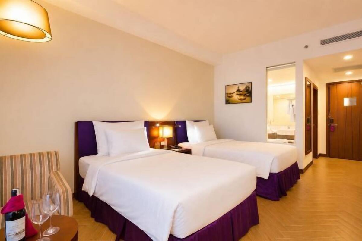 Habitación de hotel con dos camas, piso de madera, un cuadro en la pared y una puerta que da a un baño.