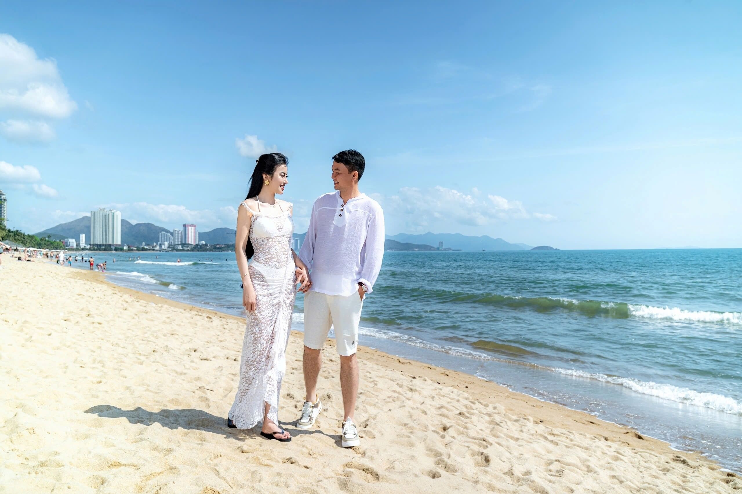 A beach with a couple standing, a clear sky, and buildings in the background.