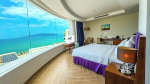 A hotel room with a large window offering a view of the sea and a herringbone wooden floor.