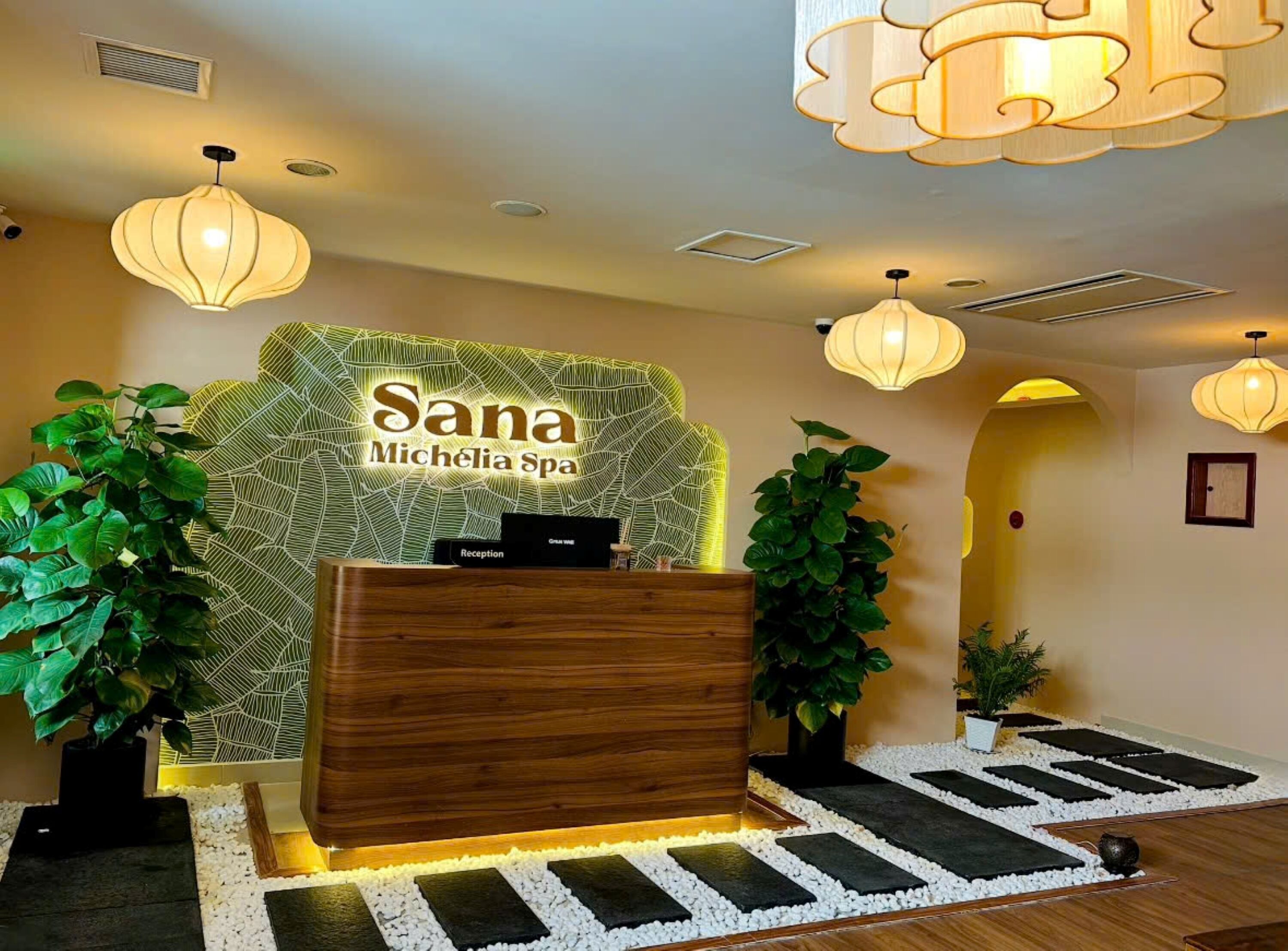 Un mostrador de recepción con un cartel que dice 'Sana Michele Spa', rodeado de plantas en macetas y un muro decorativo.