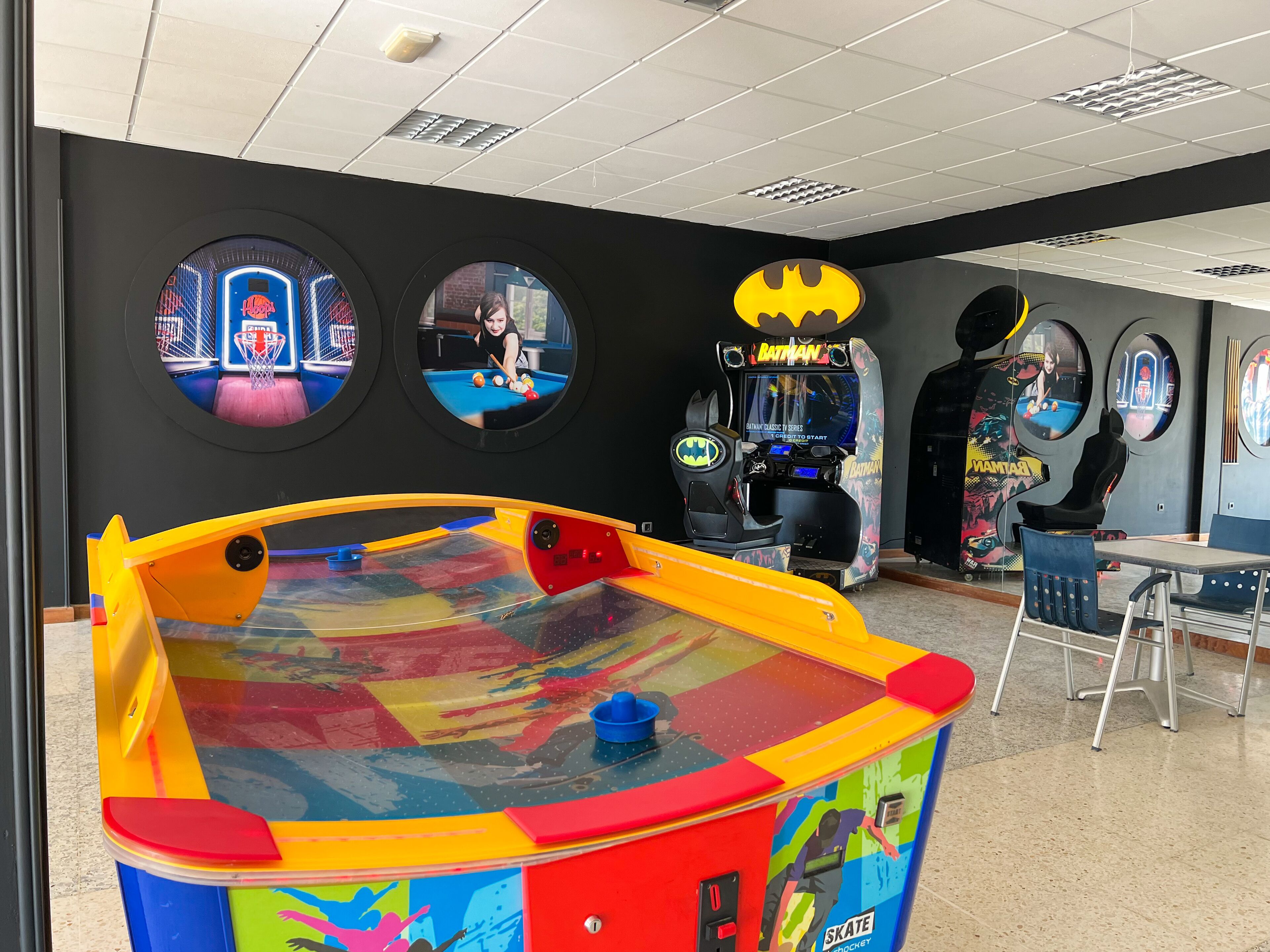 Een kleurrijke speelhal met diverse spelautomaten, waaronder een pooltafel en een Batman-thema spel.
