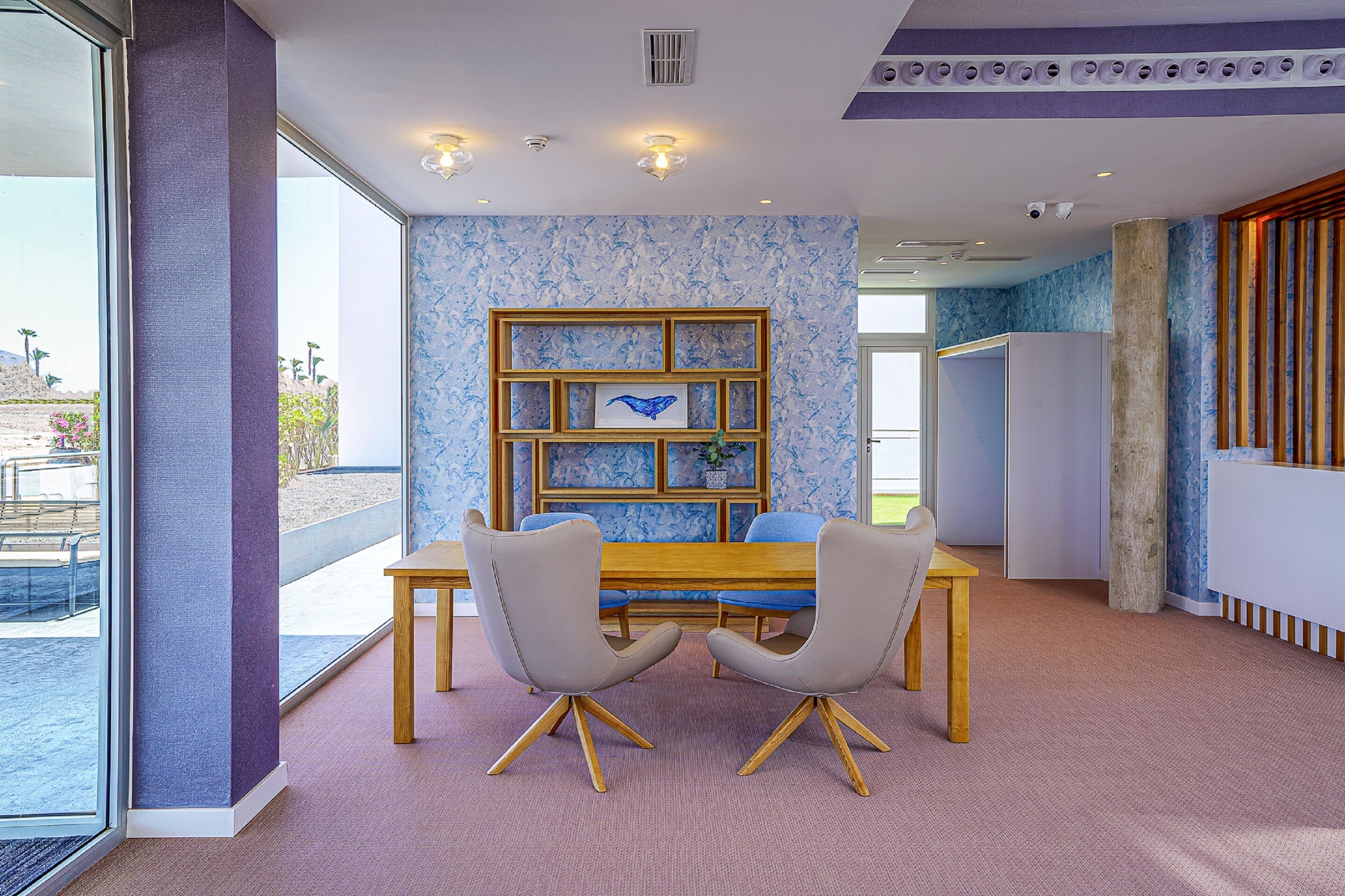 Un comedor moderno con una mesa de madera, dos sillas grises y una estantería con marco azul.