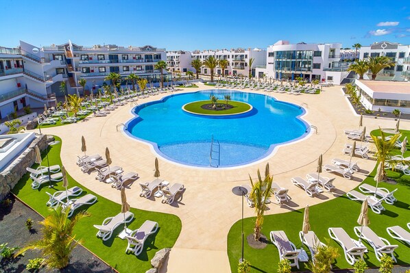Un resort con piscina central, tumbonas y palmeras.
