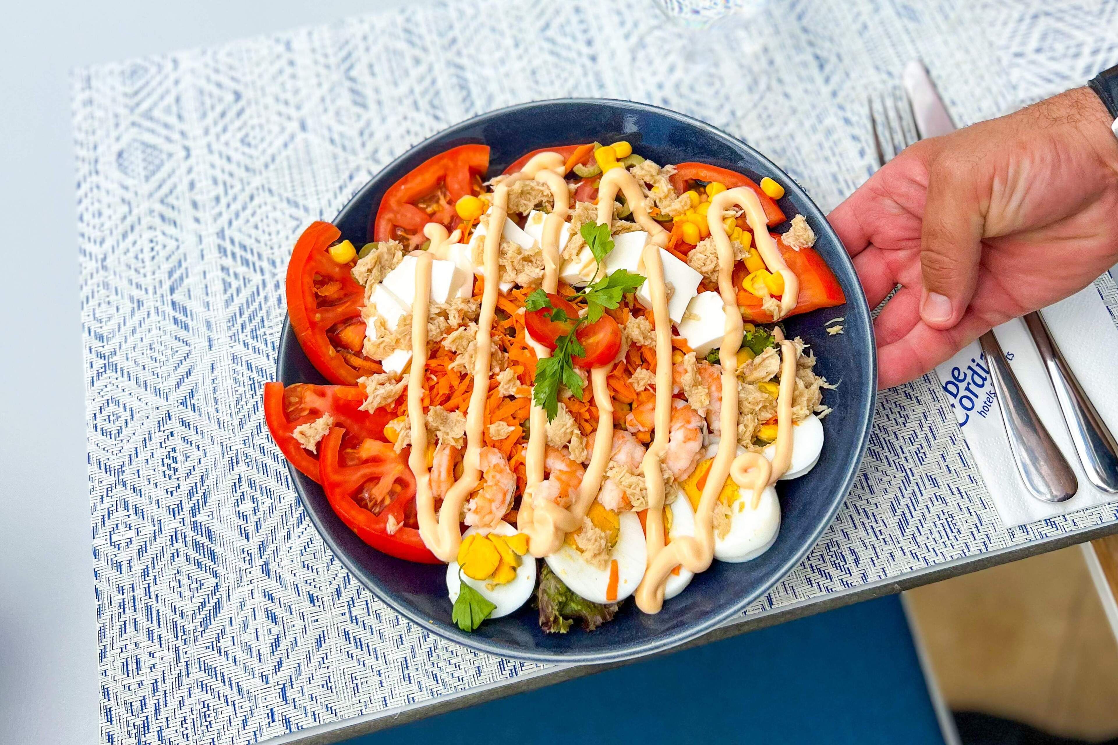 Un tazón de ensalada con diferentes ingredientes y una mano sosteniéndola.