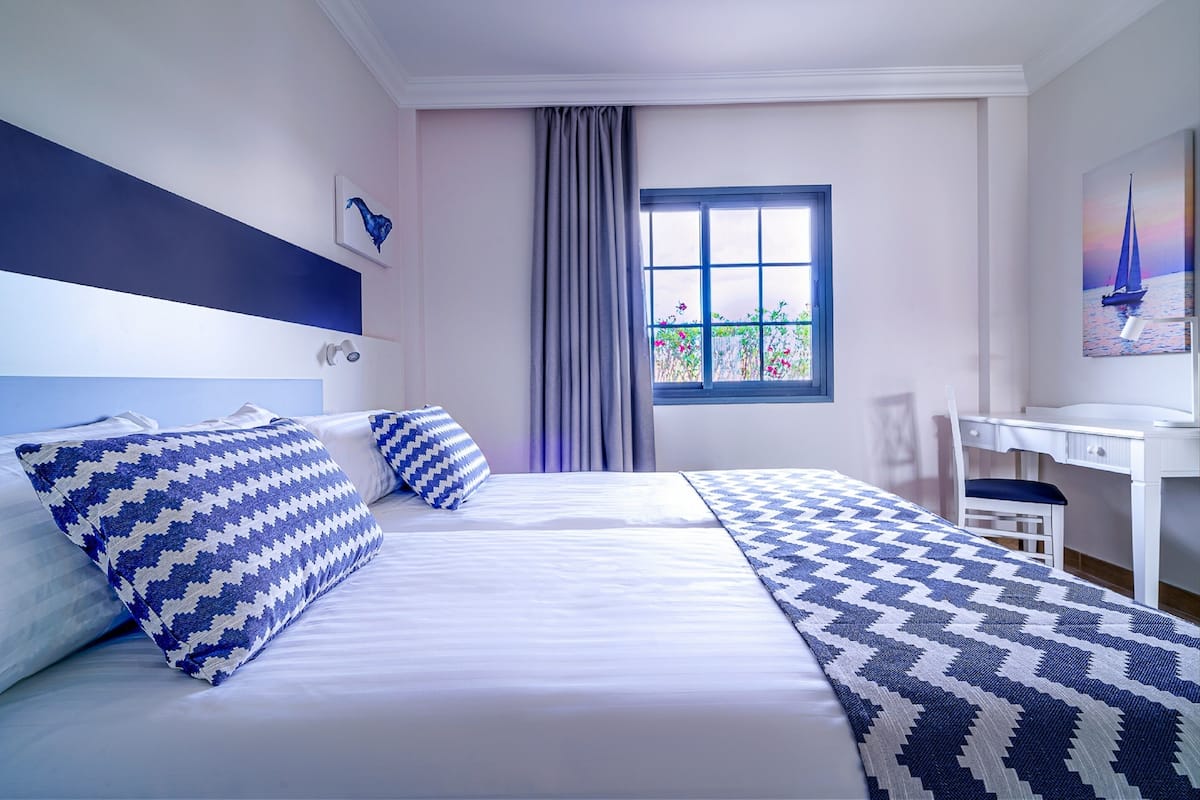 A hotel room with a large bed, a desk, and a window with a view of flowers.