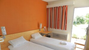 A hotel room with two single beds, a wooden headboard, a small bedside table with a lamp, a window with striped curtains, and a view of greenery outside. - The Originals Access, Hôtel Tulle (Tulle)
