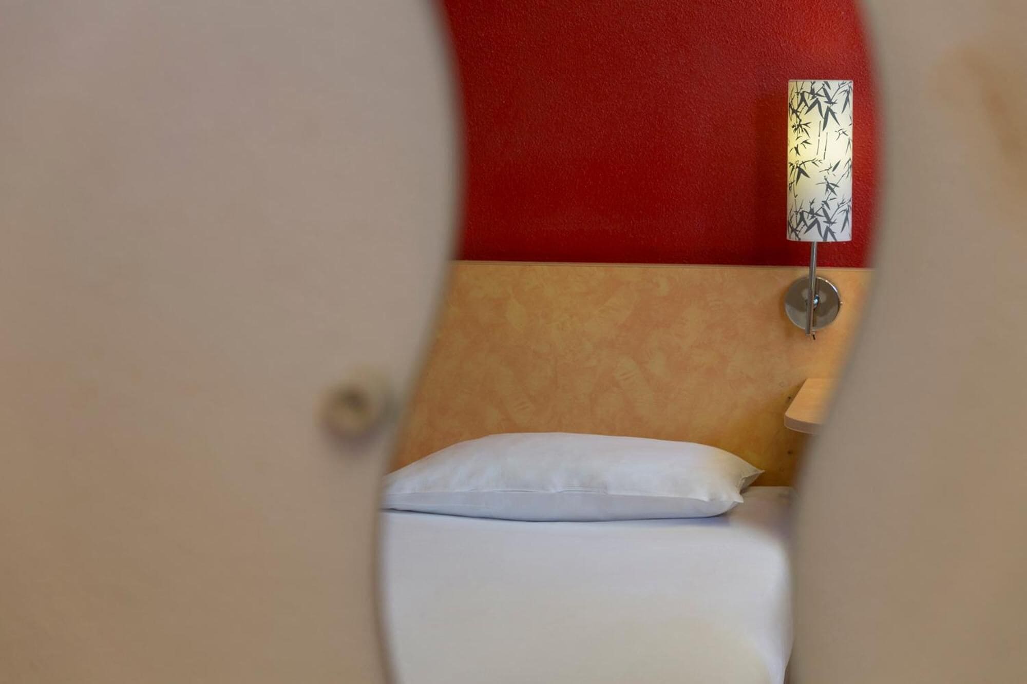 Una camera d'albergo con un letto, una parete rossa e un lampadario a muro.