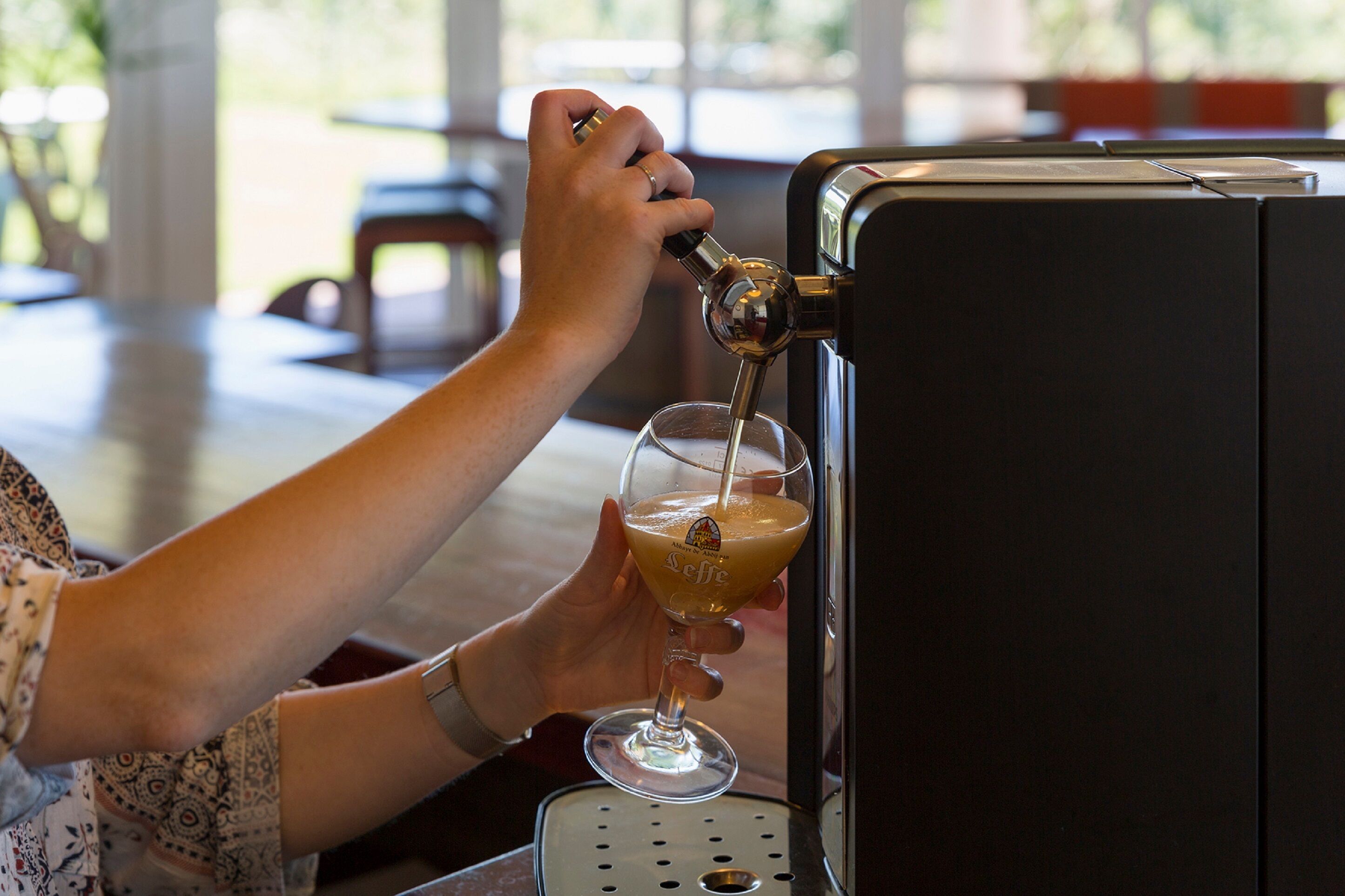 A person pouring a drink from a tap into a glass.