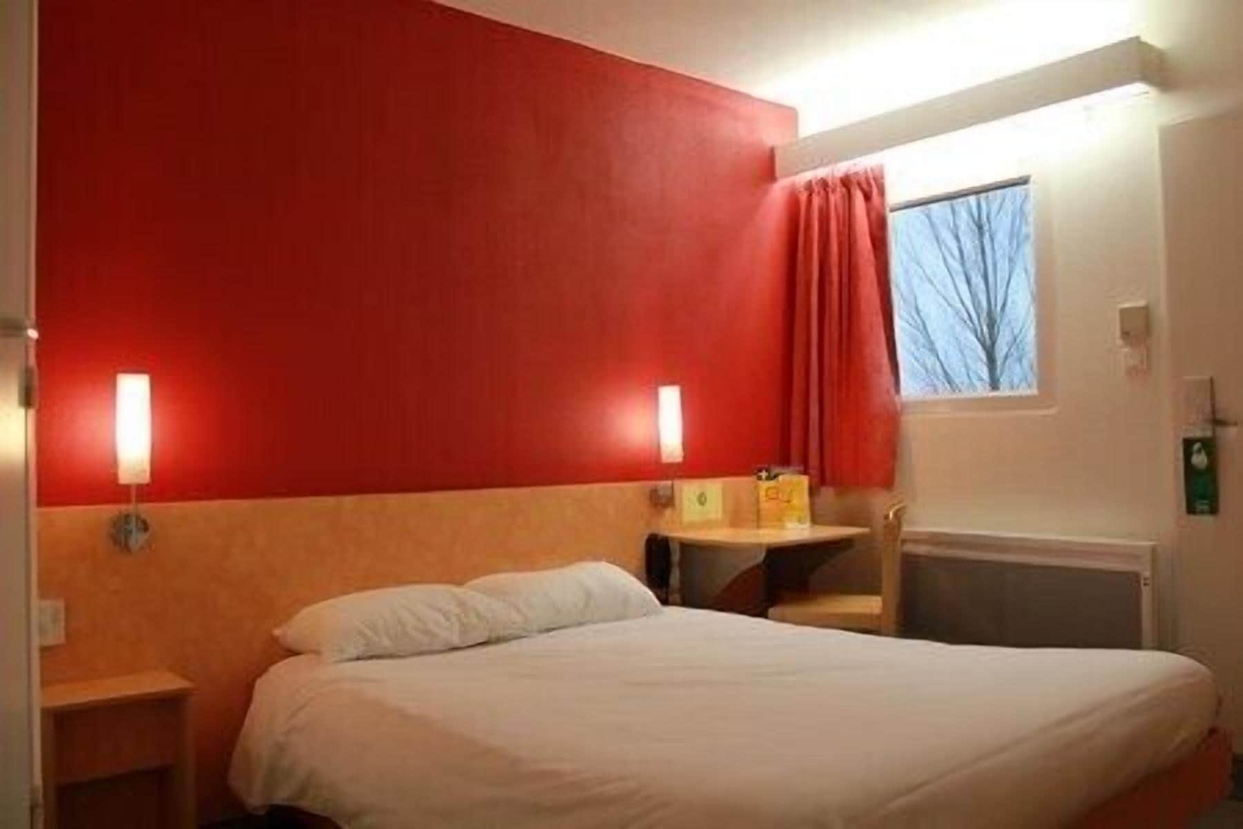 Habitación de hotel con una cama, una mesita y una ventana que da a árboles.