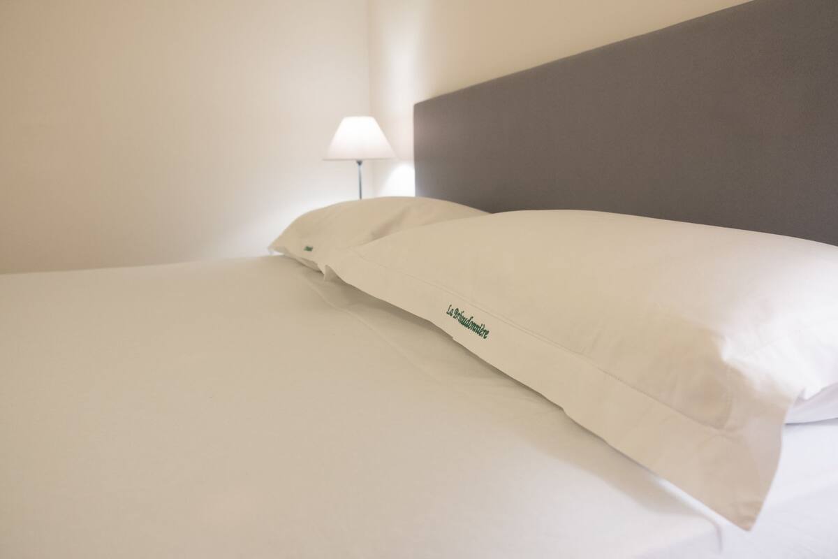 A neatly made bed with white linens and a pillow with a logo.