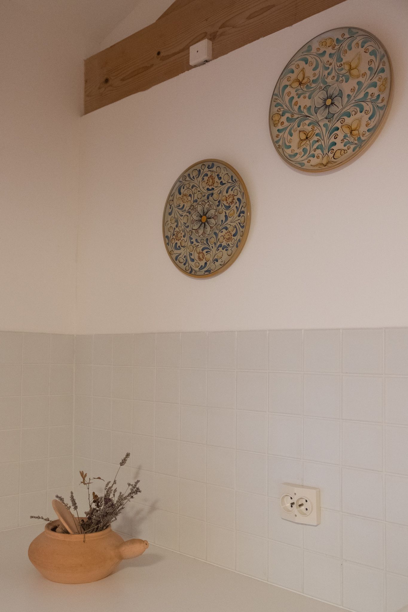 Una cocina con paredes de baldosas blancas, techo de madera y un plato decorativo en la pared.