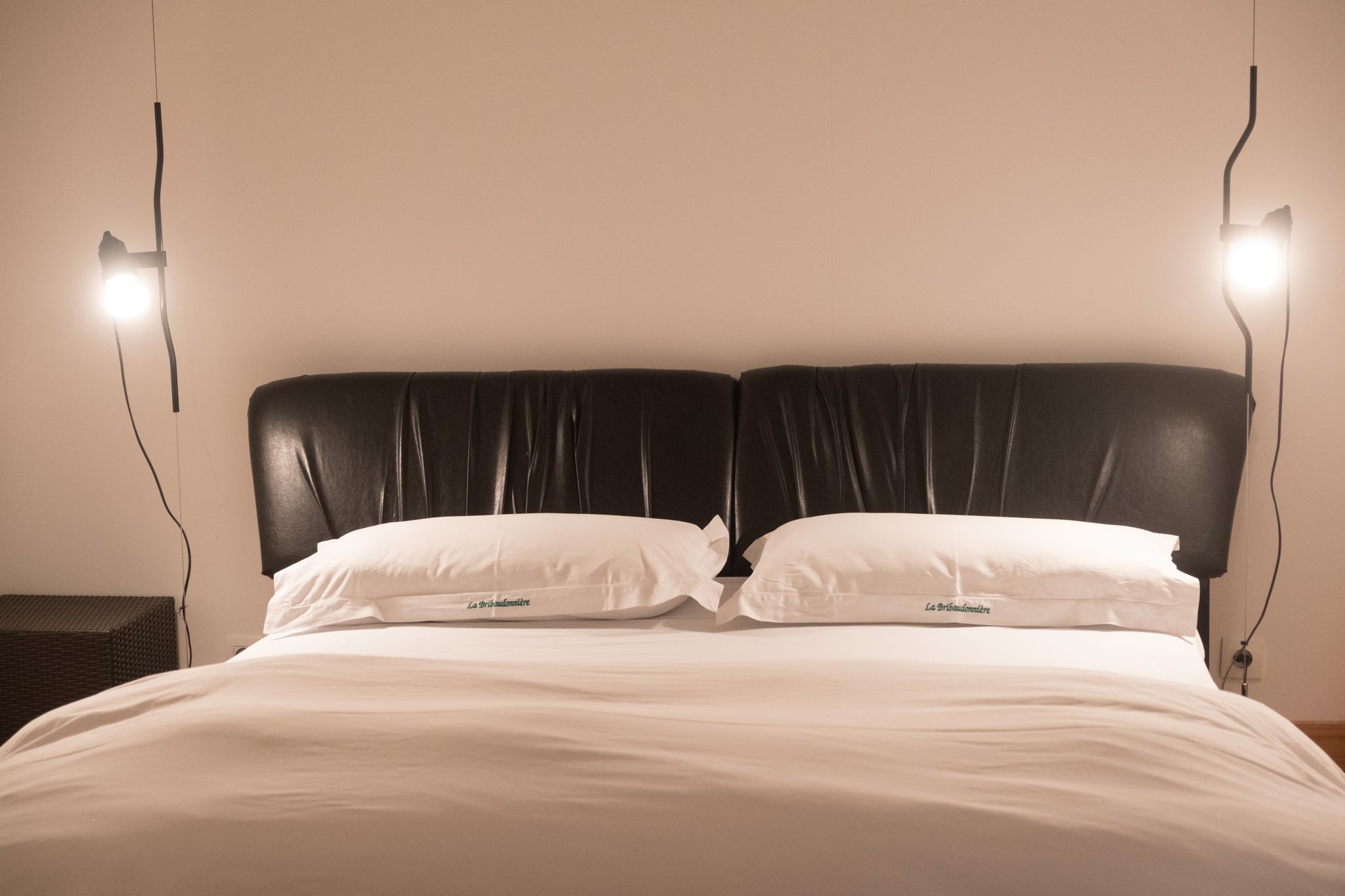 Una cama con cabecera negra, dos almohadas blancas y dos lámparas de noche.