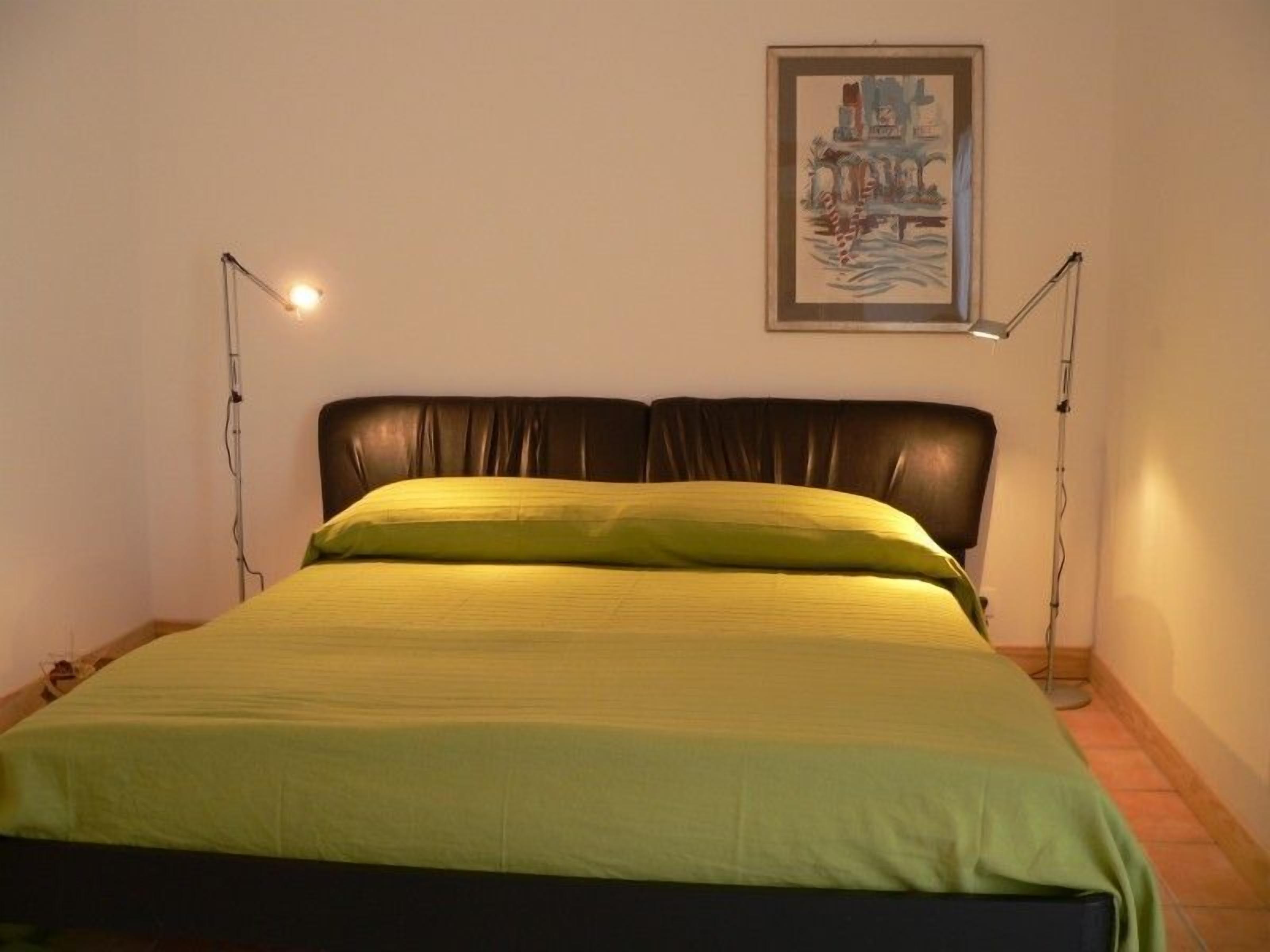 A bed with a green bedspread and a brown headboard, flanked by two bedside lamps.