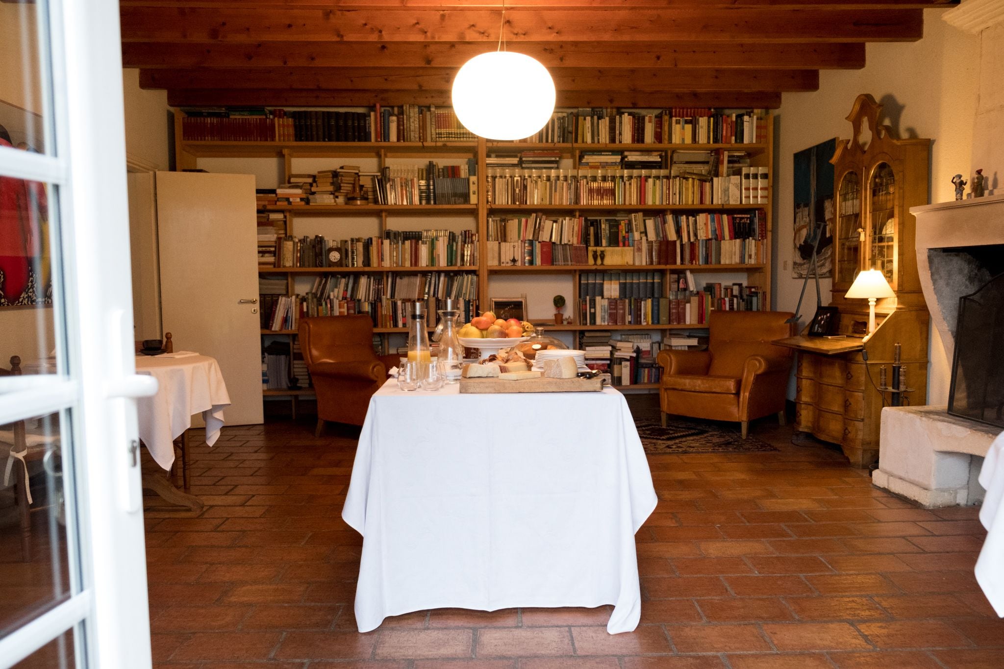 A cozy room with a dining table set for a meal, surrounded by bookshelves filled with books, a fireplace, and a wooden ceiling.