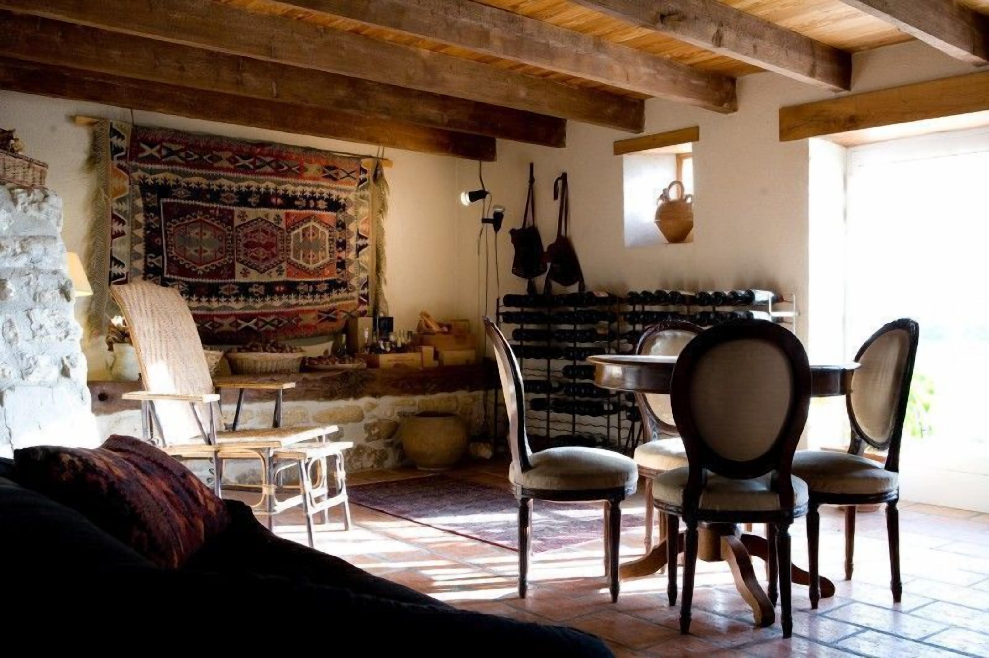 Un interno rustico con travi a vista in legno, un muro in pietra, un arazzo decorativo, una zona pranzo con sedie e una cantina per vini.