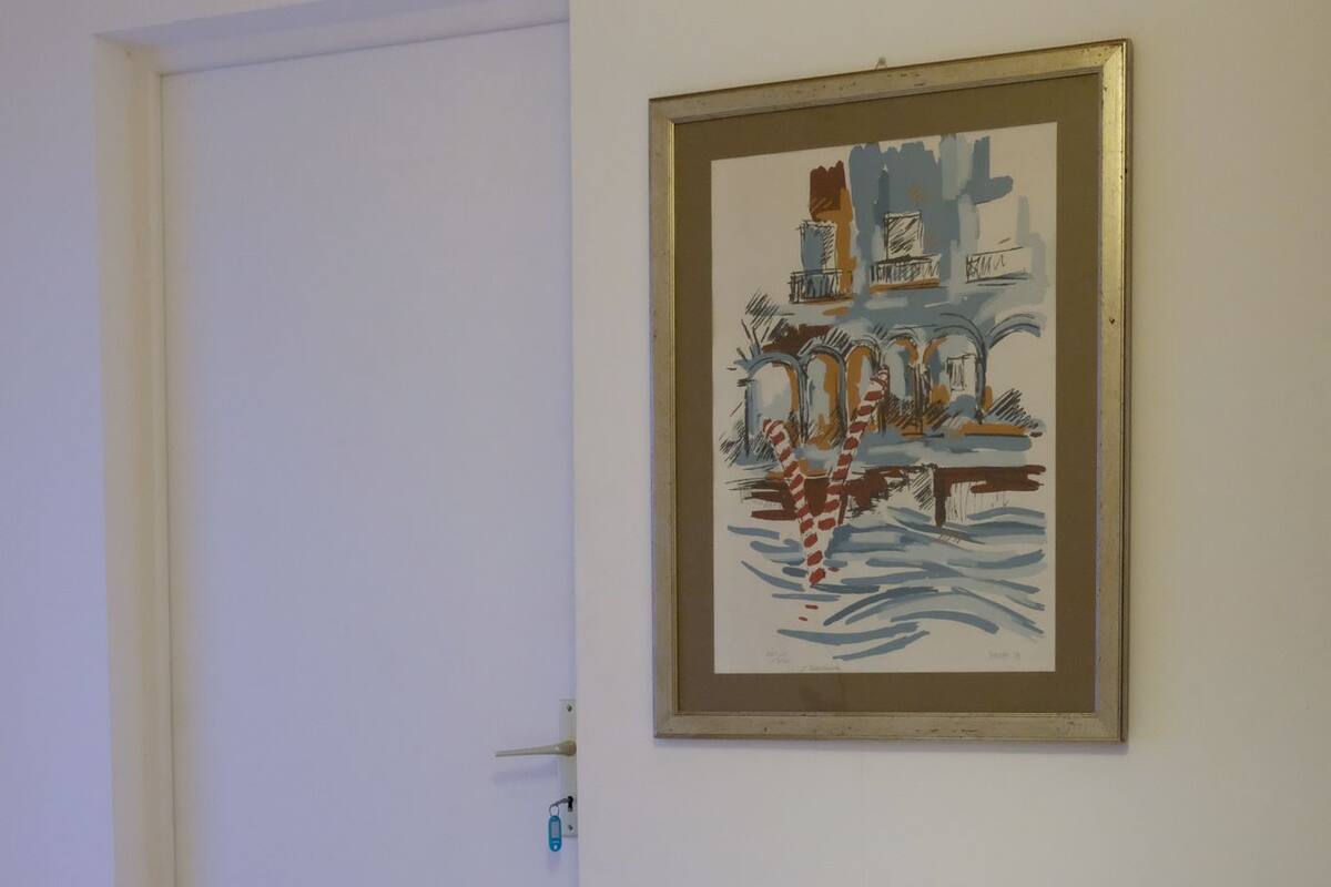A white armchair in a room with a white door and a framed painting on the wall.