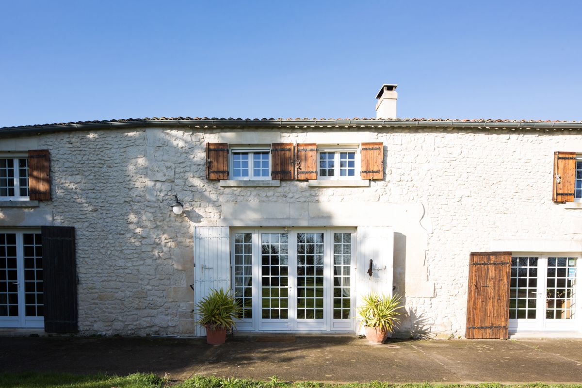 A stone building with a white facade, wooden shutters, and a central entrance with glass doors.