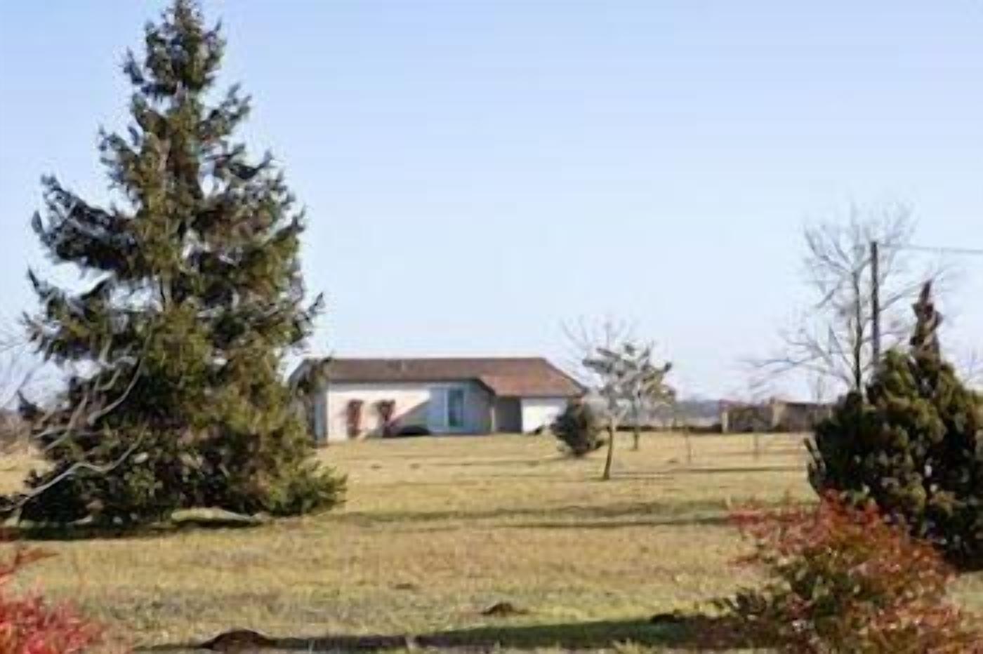 A single-story house with a sloped roof, surrounded by a grassy yard and several trees.