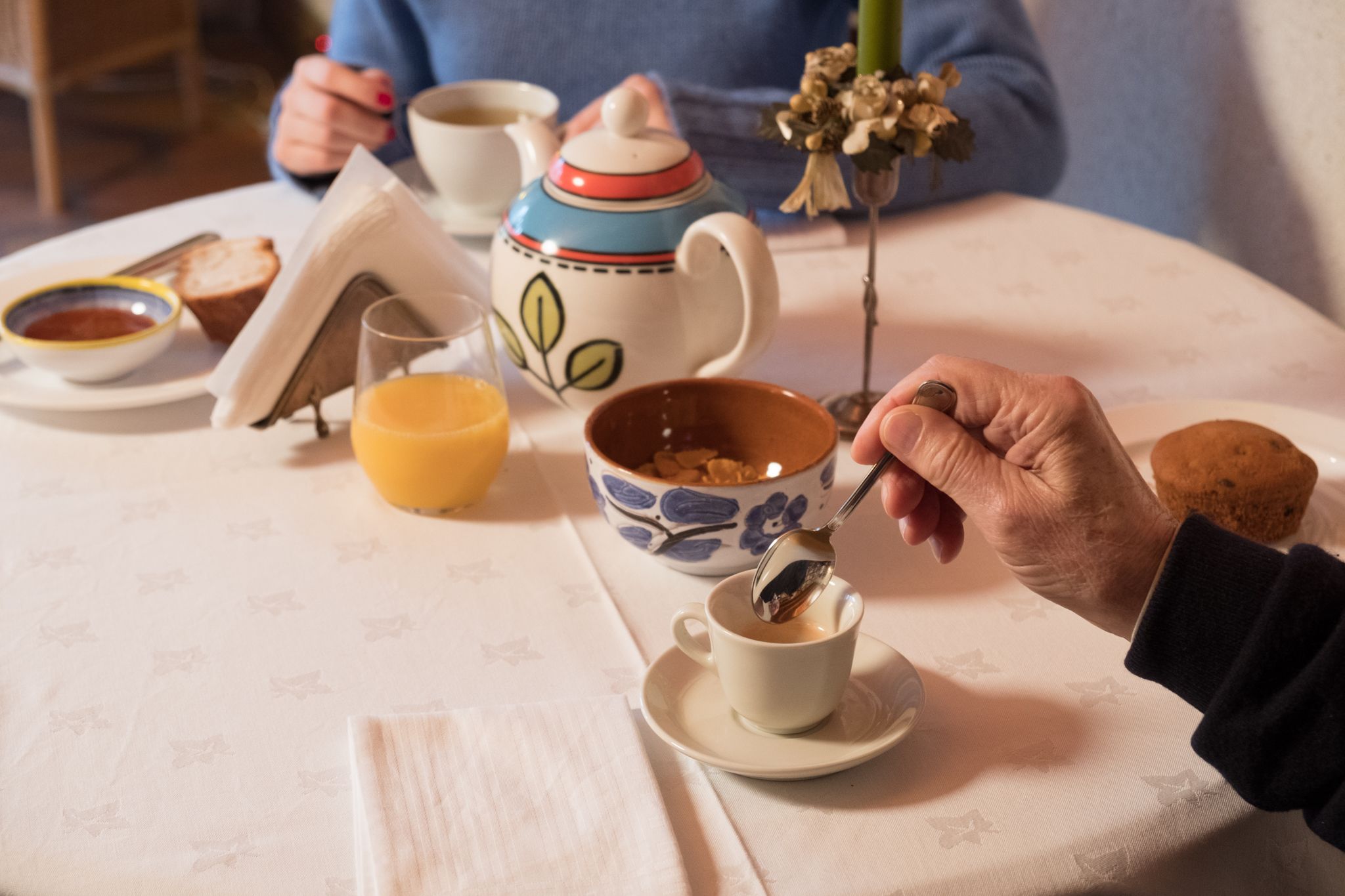 A dining table with a cup of coffee, a teapot, a bowl of cereal, and a muffin.