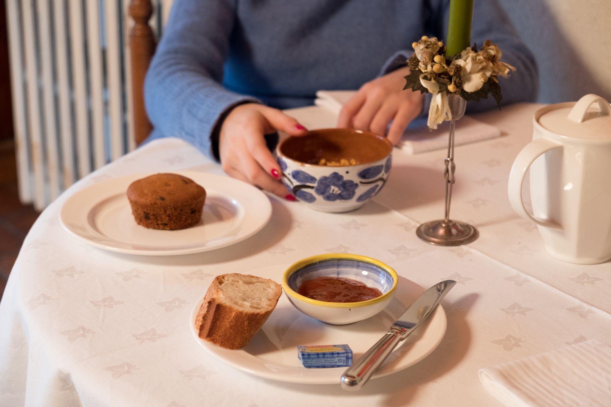 Uma mesa com um muffin, uma tigela de geleia, uma faca, um pedaço de pão e um pequeno vaso com flores.