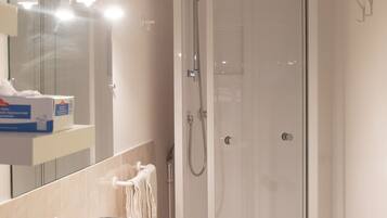 A bathroom with a white sink, a glass shower enclosure, and a mirror with lights.