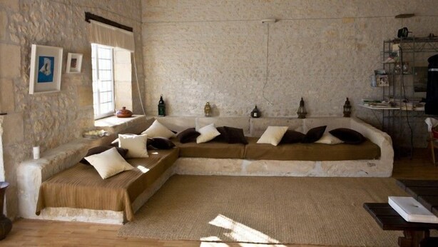 A cozy room with a stone wall, a sofa with cushions, a small table, and a shelf with items. - La Bribaudonnière (Saint-Palais-de-Phiolin)